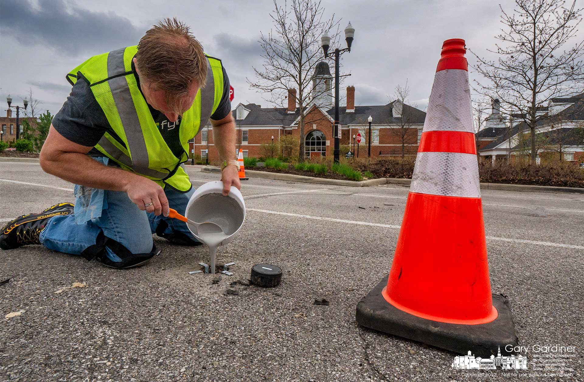 An engineer pours a liquid hardener into one of the parking sensor holes behind city hall as part of a project to upgrade sensors in city lots with an existing system that feeds an app to indicate empty parking spots. My Final Photo for April 26, 2022.