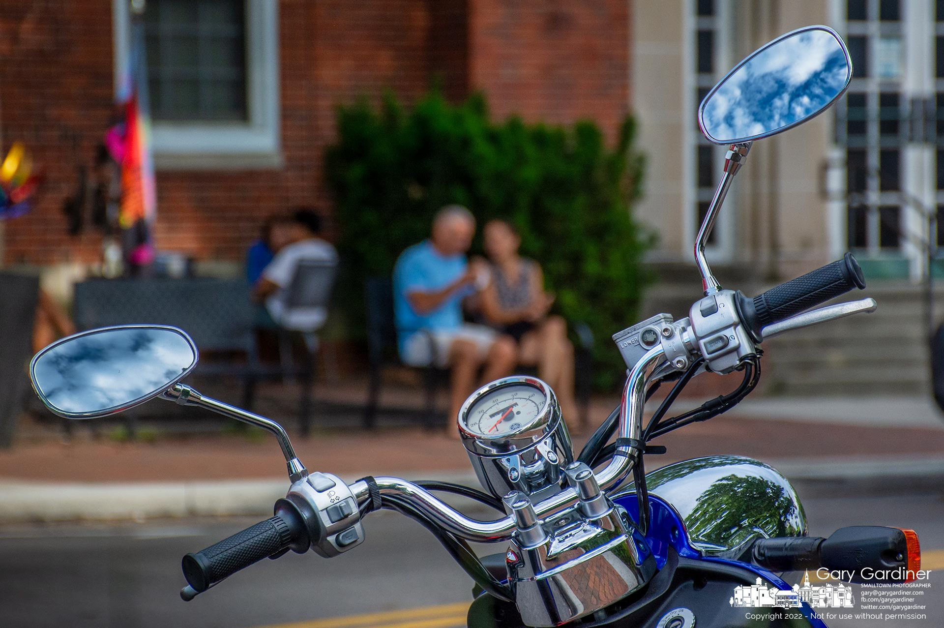 A blue sky with light clouds is reflected in a scooter's rear-view mirrors from its parking spot across from Java Central where couples are enjoying themselves on the brick walkway and patio. My Final Photo for August 5, 2022.