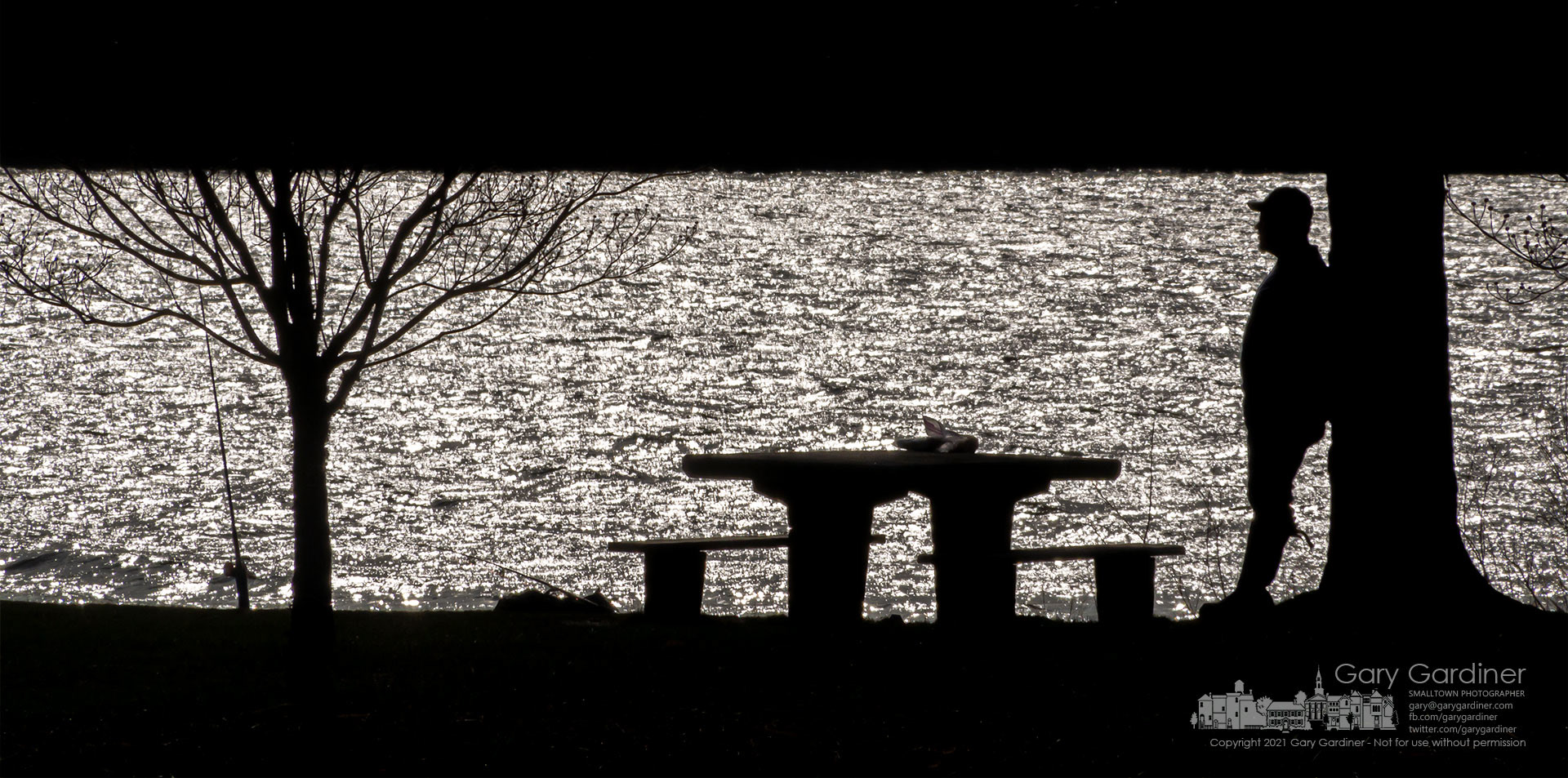 A fisherman leans against a tree along the shoreline at Hoover Reservoir where he's cast his bait into water sparkling in the morning sun. My Final Photo for April 3, 2021.