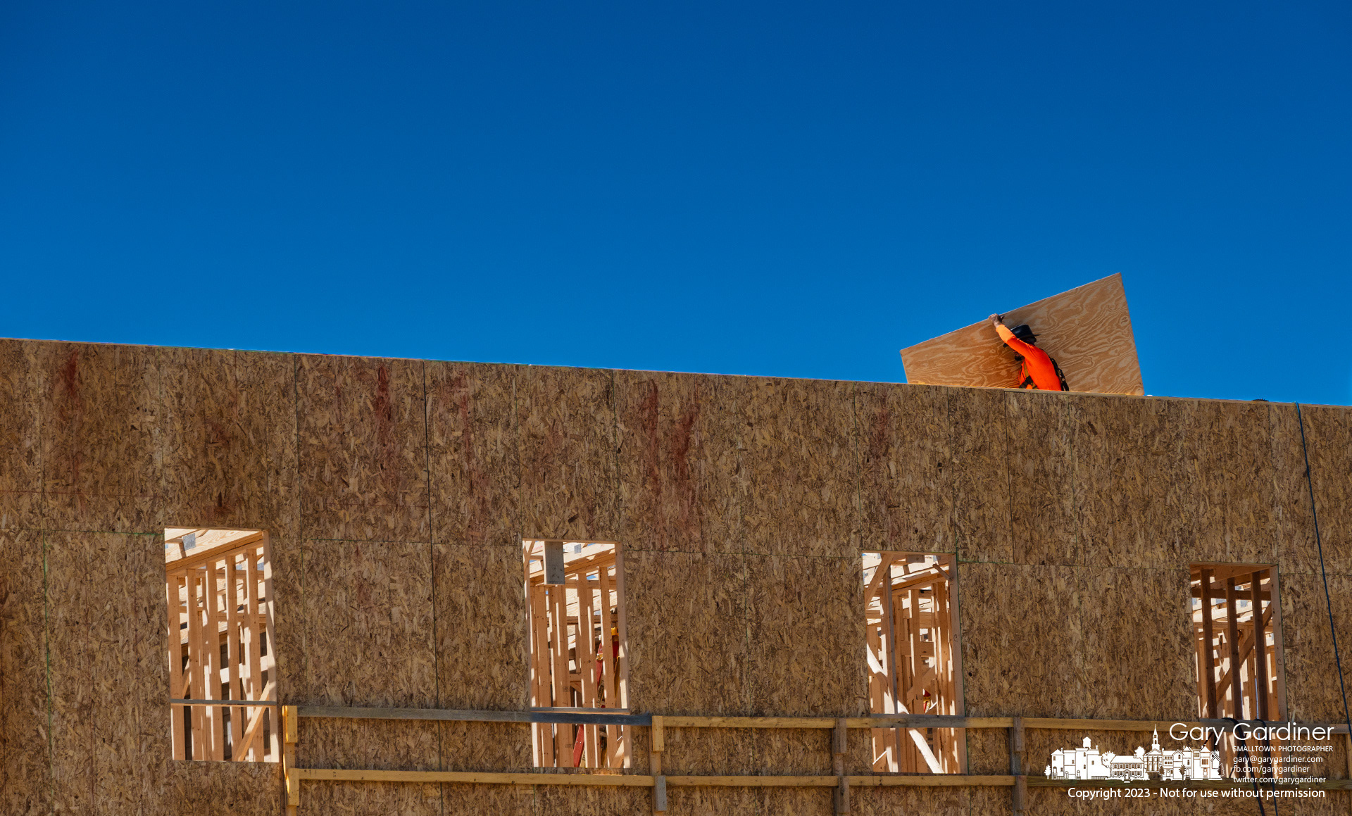A carpenter carries plywood sheathing across the top floor ceiling of a three-story building on West College is being built. My Final Photo for August 31, 2023. 