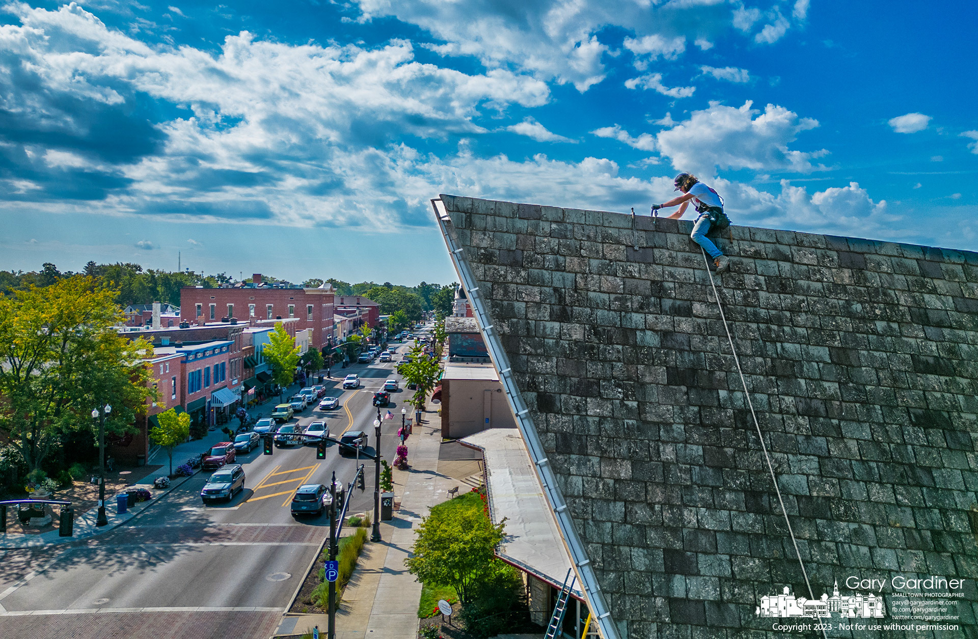 A roofer straddles the peak of the slate roof of Church of the Messiah in Uptown Westerville where he was replacing broken tiles as part of repairs to the church's roof. My Final Photo for September 6, 2023. https://bit.ly/3Euk2MF