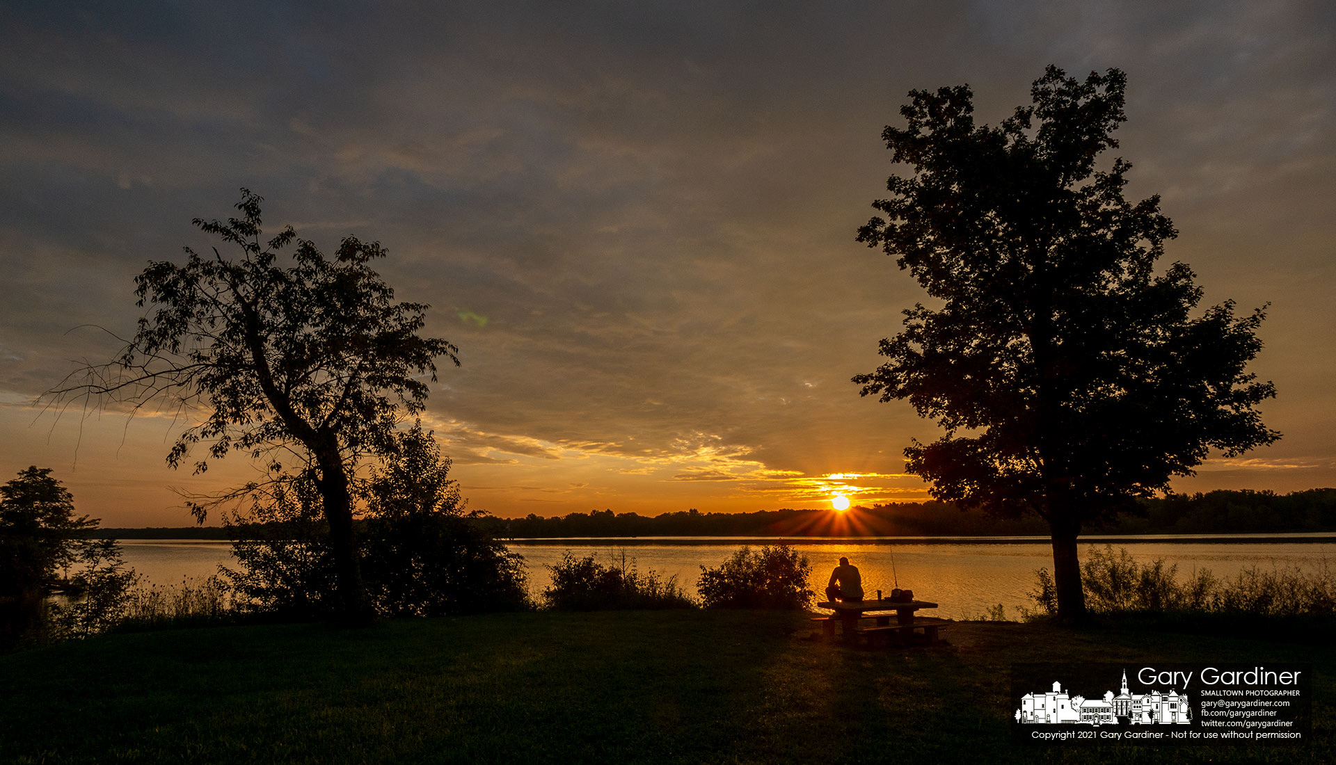 A fisherman watches his lines and the sunrise over the trees from his perch on the picnic table at the edge of Hoover Reservoir at Red Bank Marina. My Final Photo for Aug. 28, 2021.