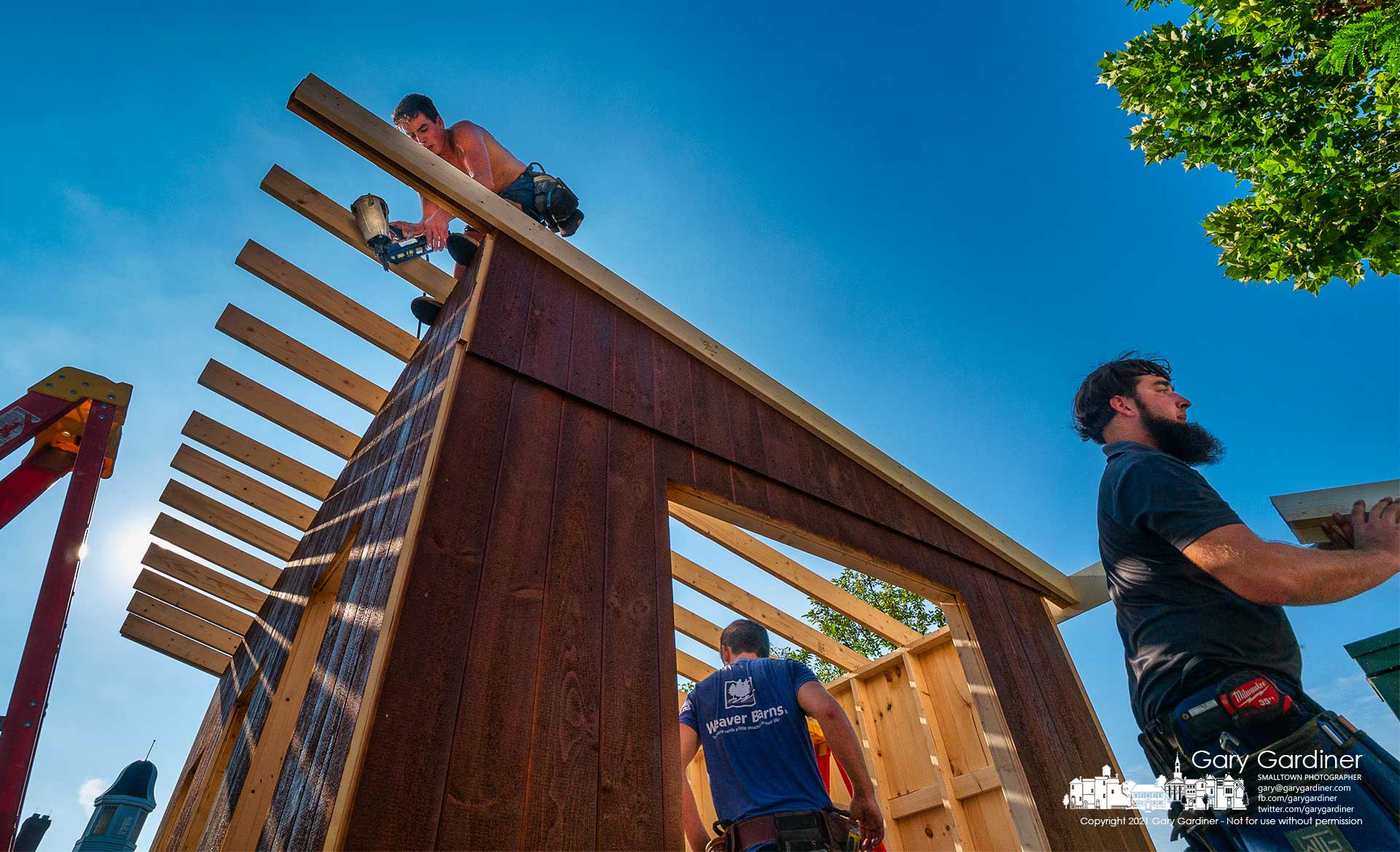 Carpenters work inside, outside, and on the roof of the storage shed being built at the rear of the First Presbyterian Church adjacent to the just-completed new city hall parking lot.