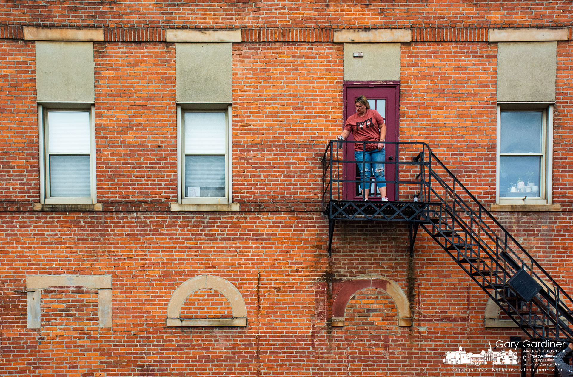 A woman spray paints the fire escape landing for the apartments above Graeter's Ice Cream after scraping away rust from the stairs. My Final Photo for October 25, 2022.