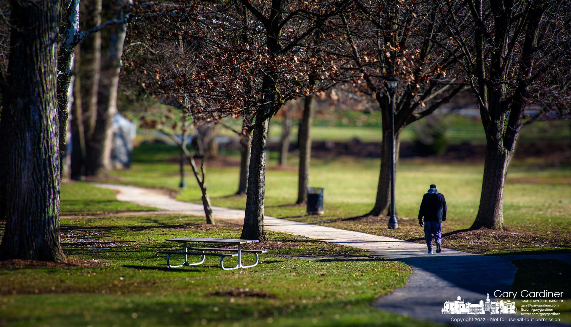 Bundled against the cold and the wind, a man walks the pathway through Alum Creek Park stepping into the sun from the shadow of the pavilion. My Final Photo for Jan. 15, 2022.