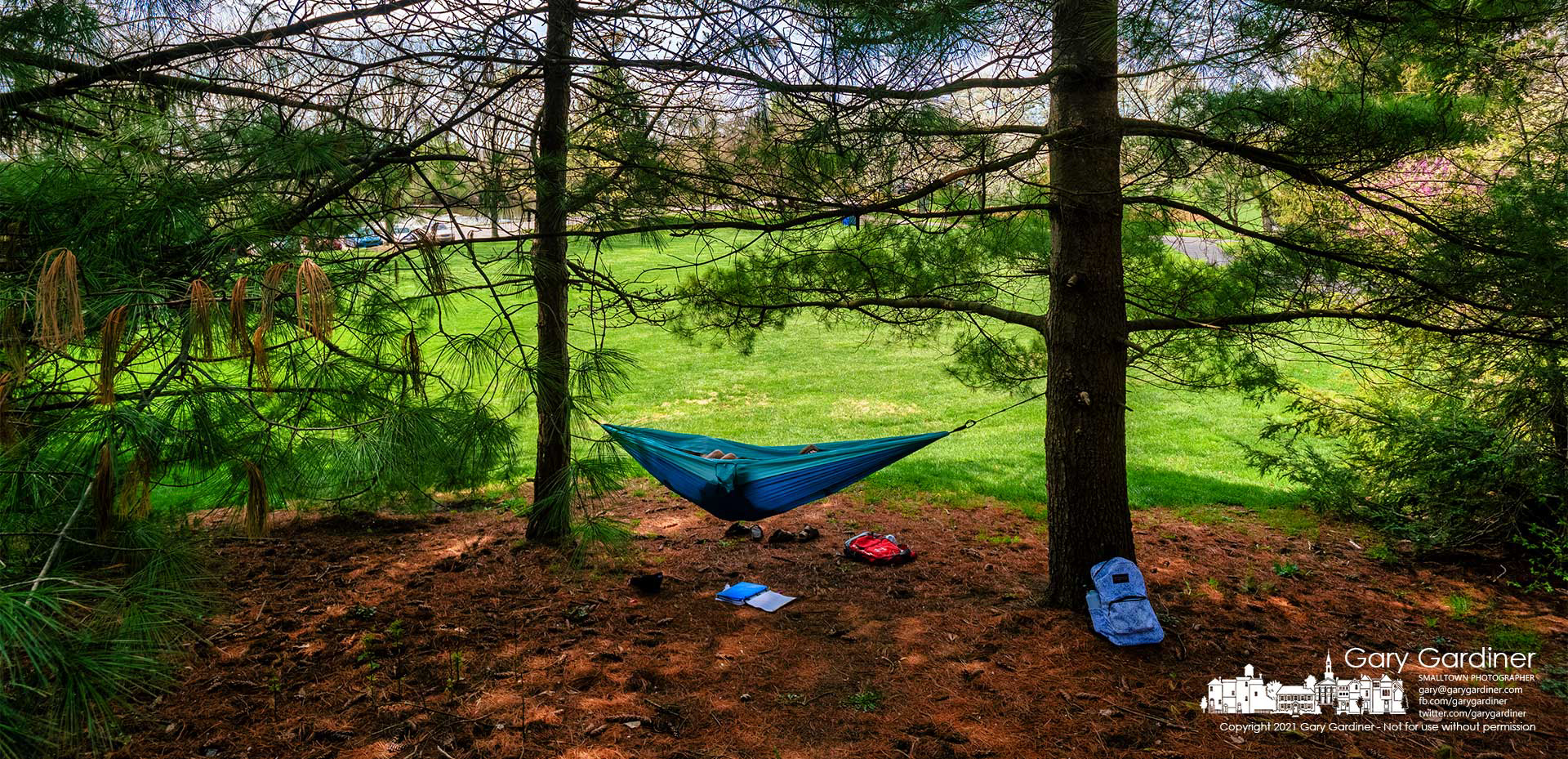 A pair of Otterbein students take advantage of noontime shade under the evergreens lining the path that leads from the school to Alum Creek Park North. My Final Photo for April 9, 2021.
