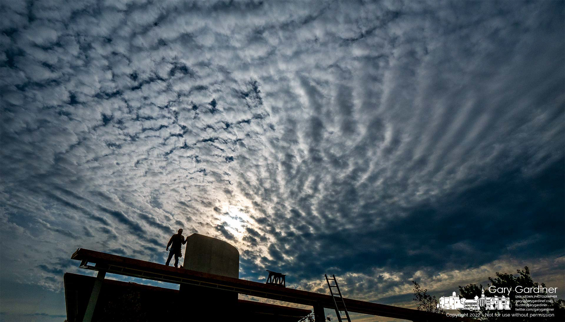 A construction worker is silhouetted against a cloudy morning sky as he helps install roofing on the Veterans Memorial under construction at the sports fields at the community center. My Final Photo for October 12, 2022.