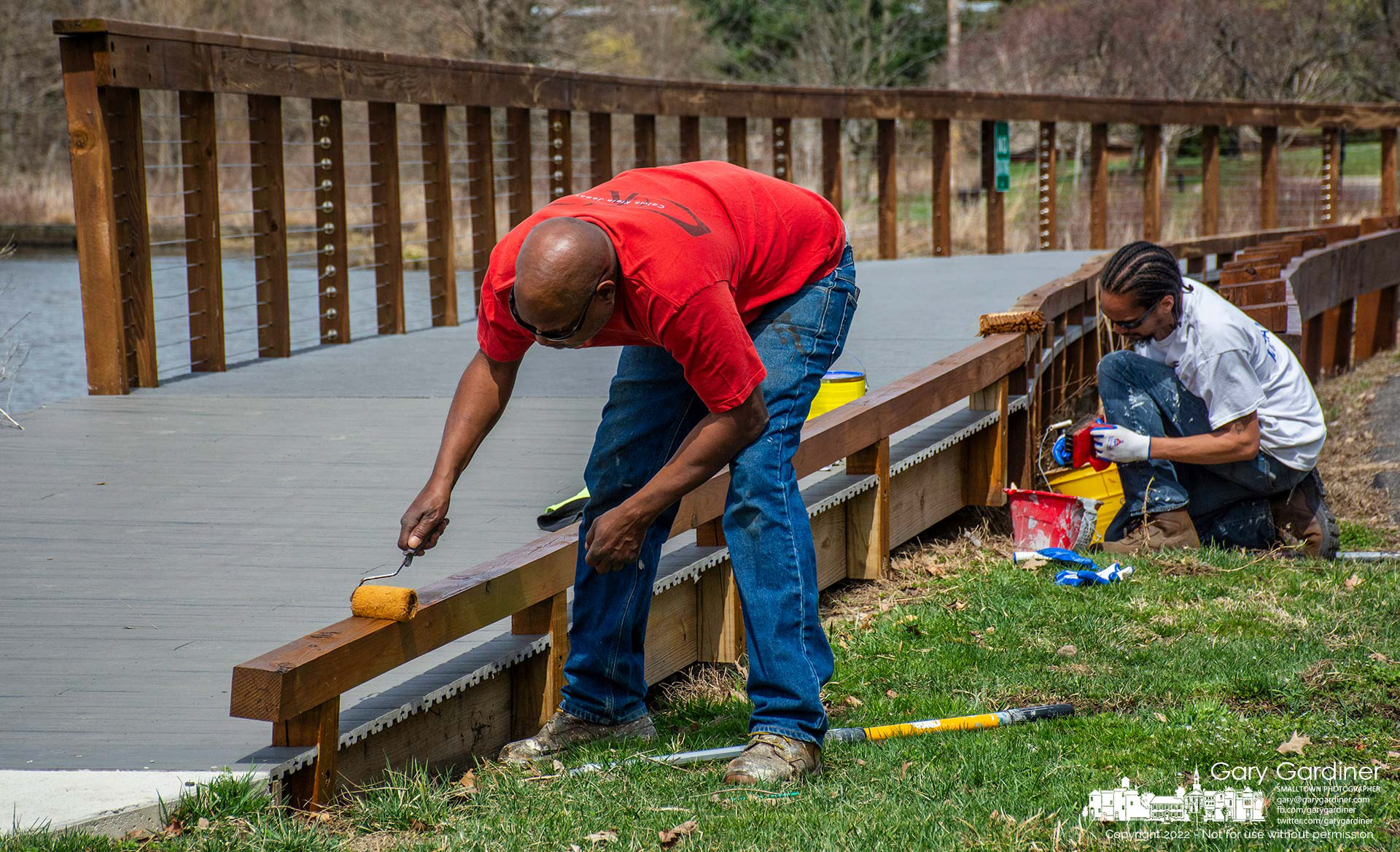 Painters apply a sealer to woodwork on the boardwalk at Highlands Aquatic Center after having completed power washing it and all the wood surfaces at the park. My Final Photo for March 30, 2022.