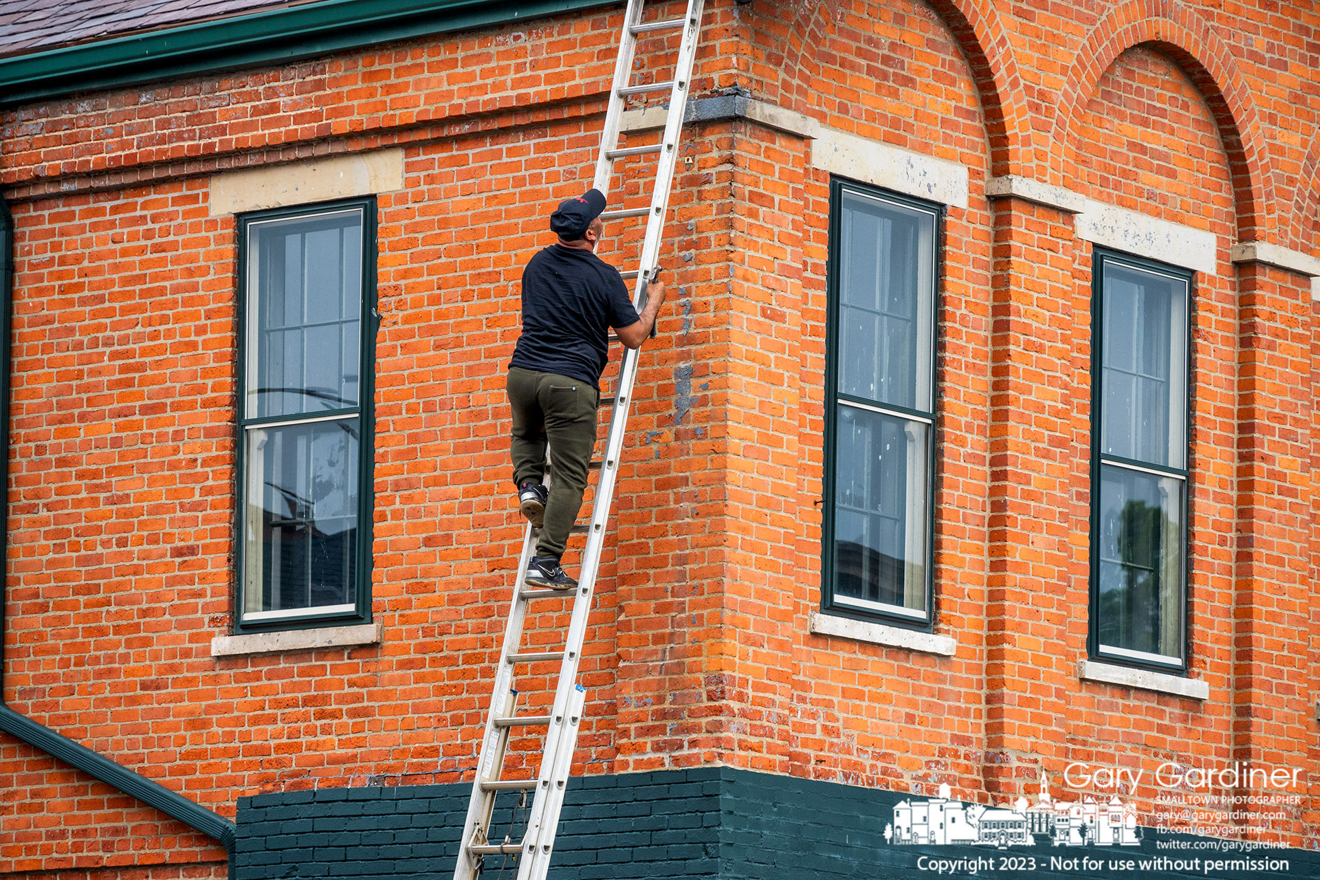 A repairman carrying a hammer checks his work after cleaning and repairing the gutter at the southeast corner of the building at State and Main with Morgan's Treasures as the first-floor business. My Final Photo for July 9, 2023. https://bit.ly/3O7L6XZ
