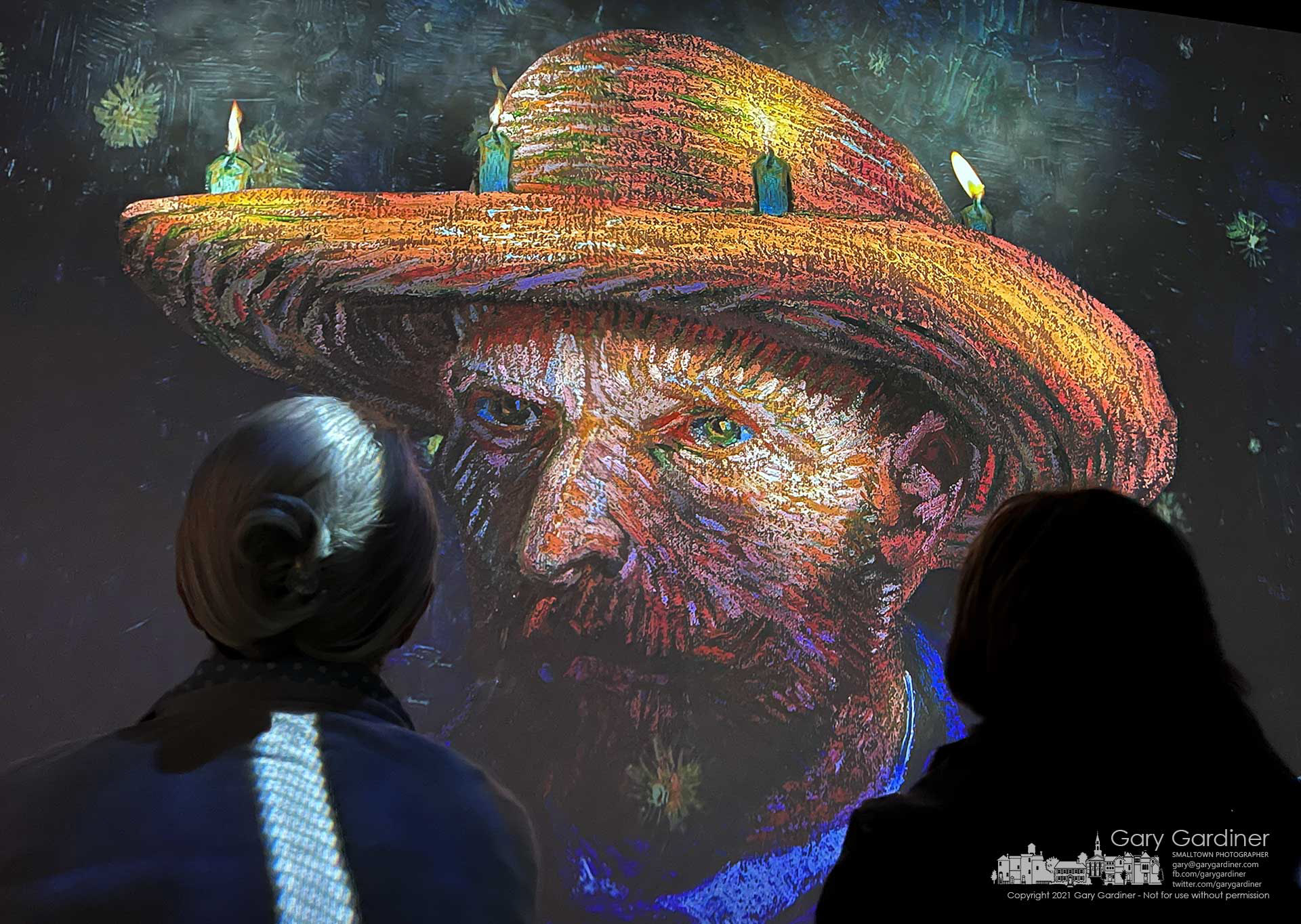 Two women study a portrait of Vincent Van Gogh during the Immersive Van Gogh multimedia show in a closed furniture store converted into a modern digital museum. My Final Photo for Nov. 9, 2021.