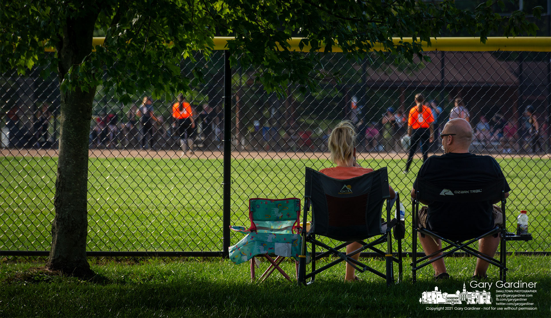 A set of parents watch a softball game at Highlands from reserved seats in the shadow of a maple tree at center field. My Final Photo for Sept. 19, 2021.