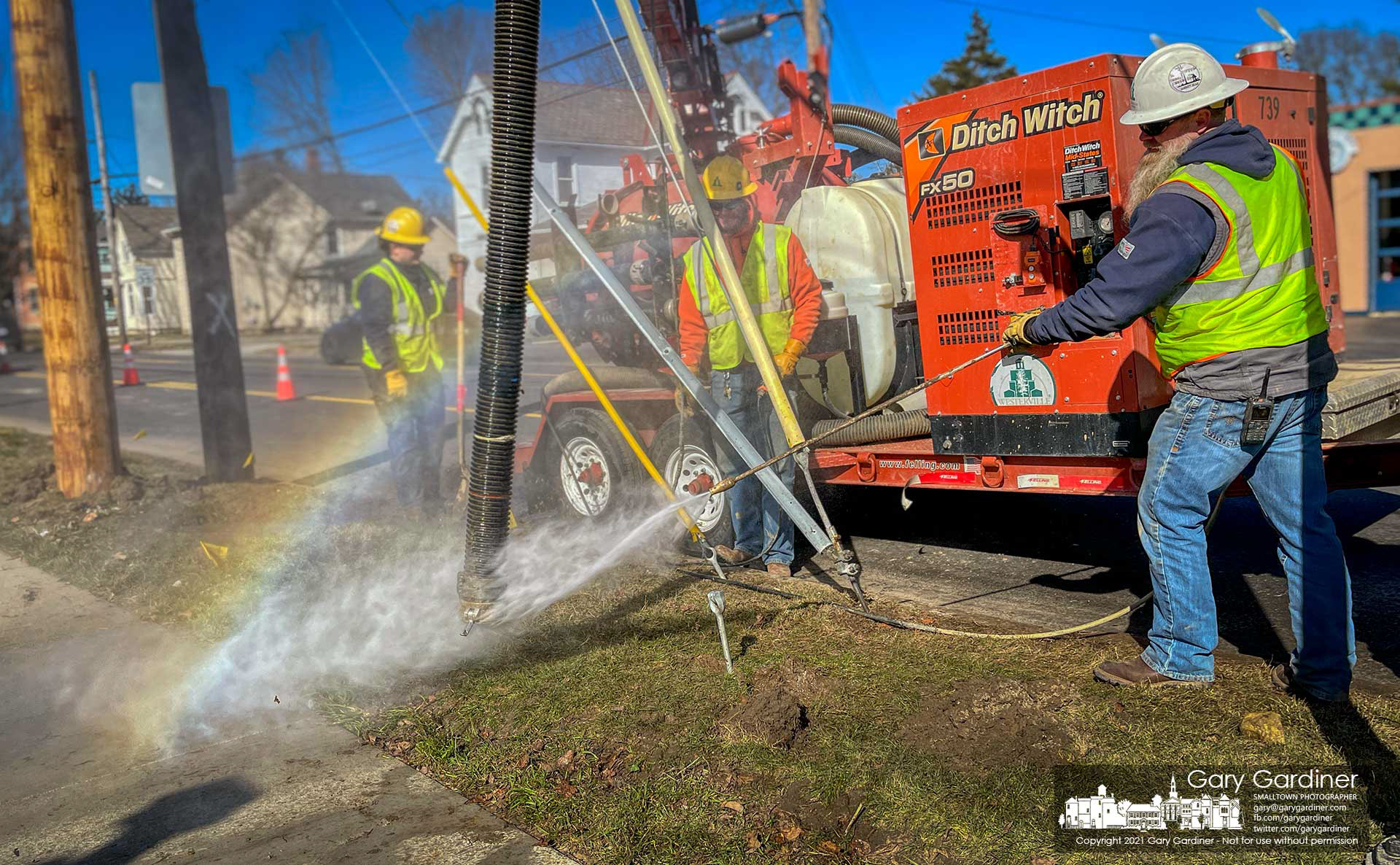 A city electric work crew creates its own small rainbow washing off a vacuum hose used to clear holes during the replacement of a utility pole in Uptown Westerville. My Final Photo for March 2, 2021.