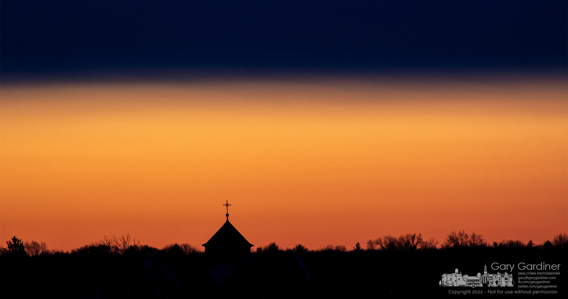 The steeple at St. Paul the Apostle Catholic Church stands above the tree line as the first light of day brightens the horizon minutes before sunrise. My Final Photo for March 13, 2022.