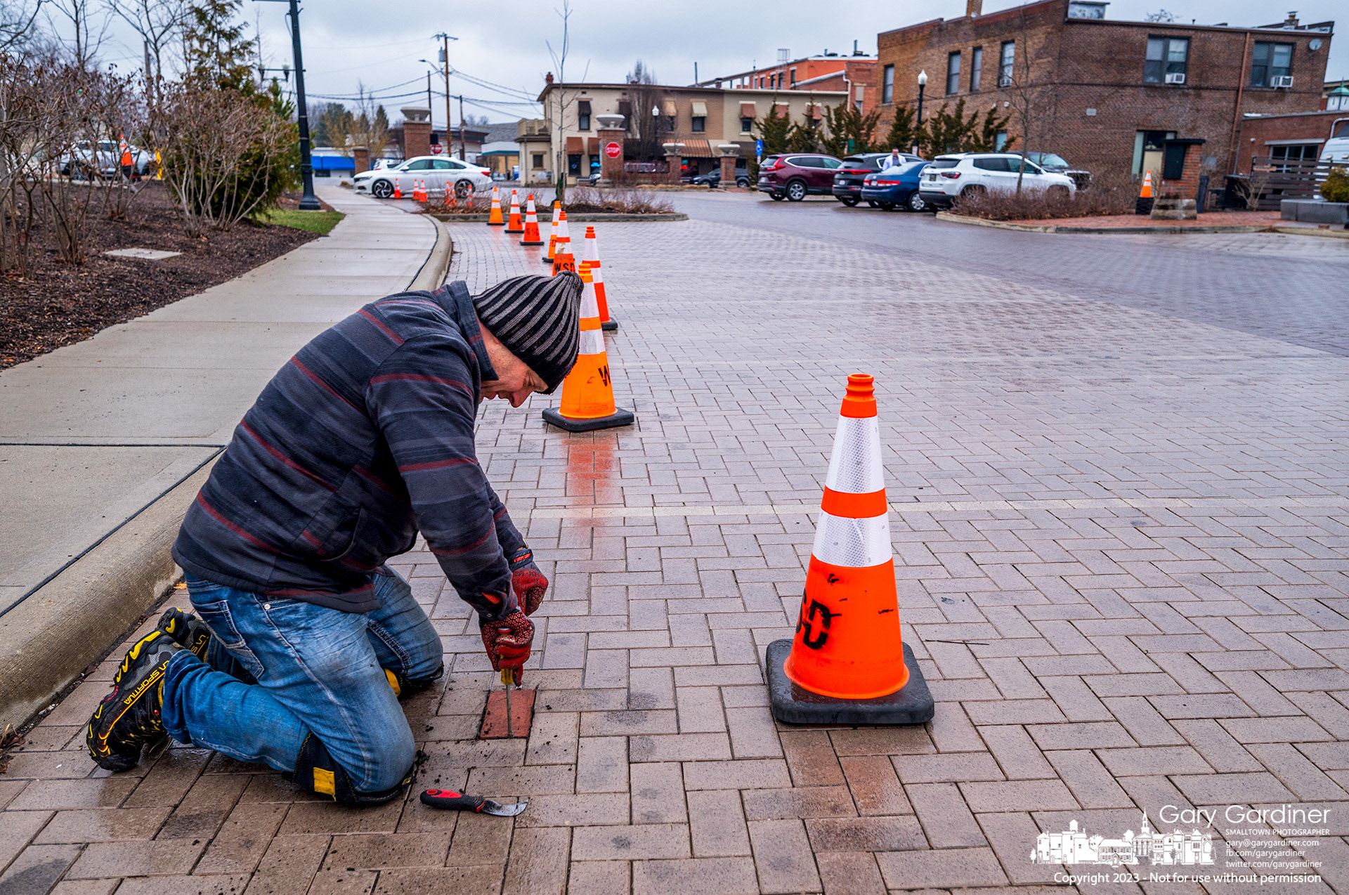 Technicians replace parking sensors in the city hall parking lot as the city upgrades the original almost two-year-old trial version of the system with longer-lasting sensors to feed information to an app detailing open parking spots in Uptown. My Final Photo for March 13, 2023. 
