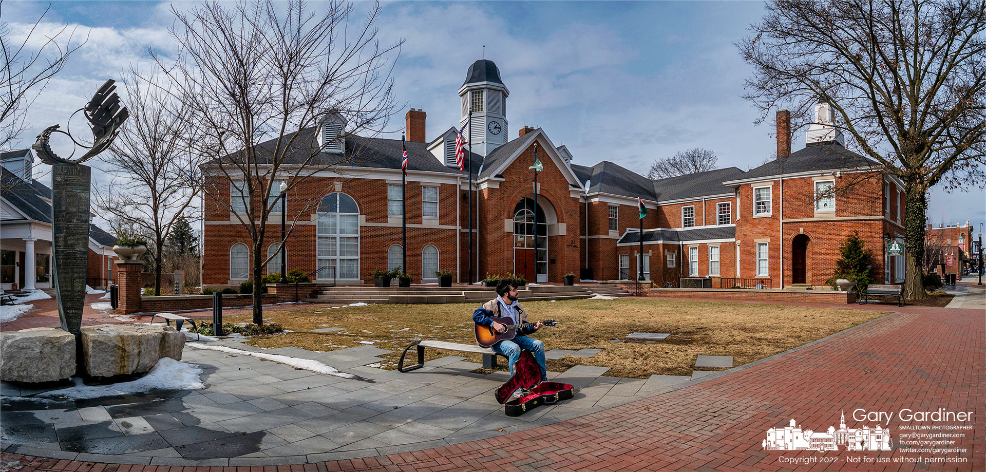 A busker sets up in front of city hall hoping that relatively warm weather and clear skies might bring out a few fanciers of guitar music and his strong voice. My Final Photo for Feb. 16, 2022. 
