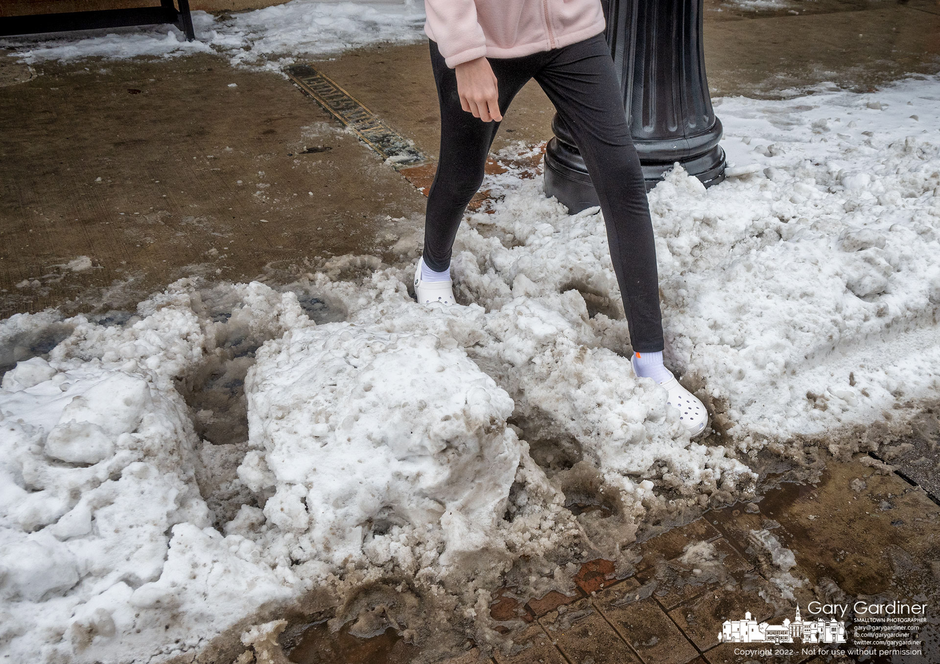 A teenager wearing Crocs steps through cold dirty slush collected at the curb in Uptown as warming temperatures and the application of ice-melting chemicals begin to melt several inches of snow and ice from a winter storm. My Final Photo for December 27, 2022.