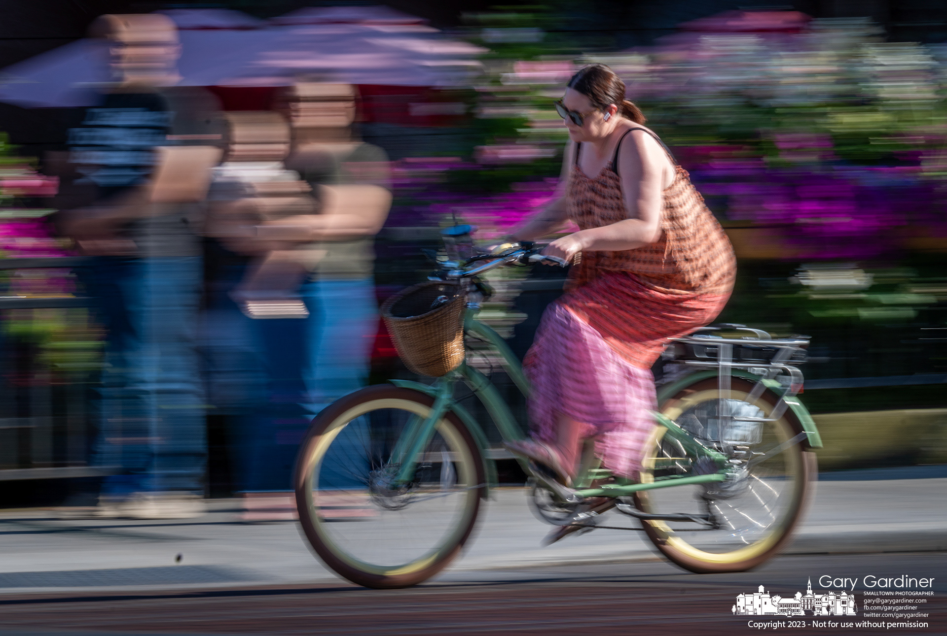 A cyclist pedals past the flowers at Jimmy V's as she works her way east along College Avenue in Uptown Westerville early Friday evening. My Final Photo for July 14, 2023.