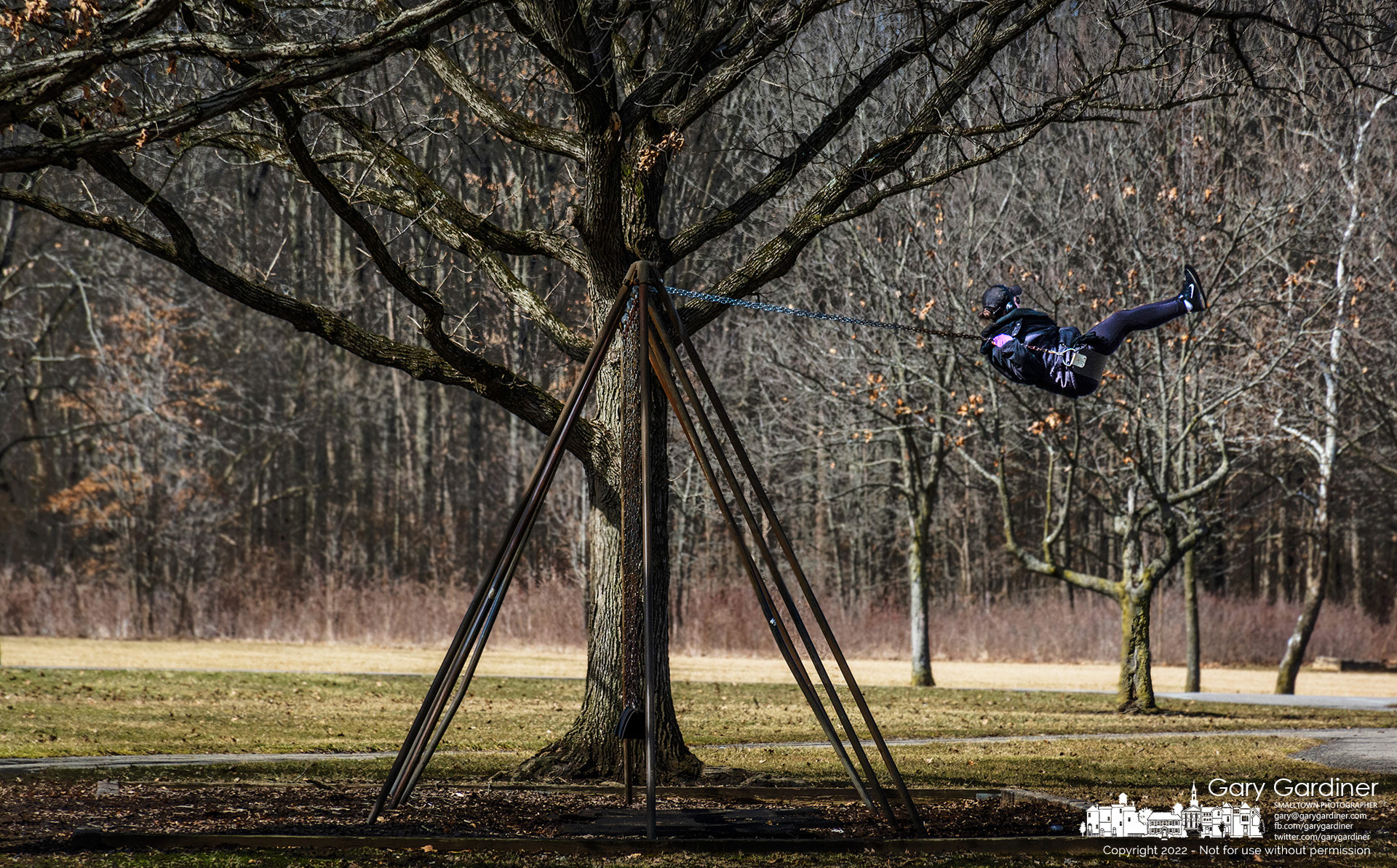 A woman reaches the apogee of her swing's forward thrust as she enjoys herself with headphones and the child-like efforts to fly on a swing. My Final Photo for March 3, 2022.