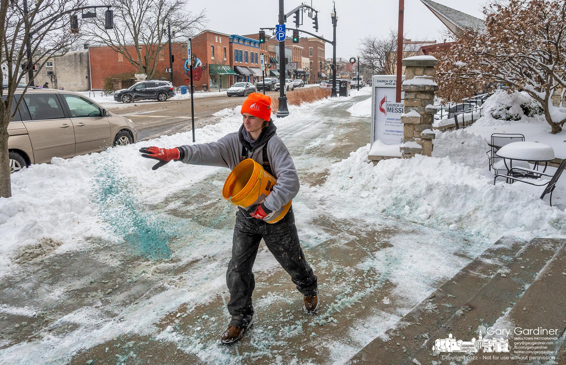 A worker spreads blue-colored deicing crystals across the Church of the Messiah entrance as the congregation arrives for Christmas Eve services at the Uptown Westerville church. My Final Photo for December 24, 2022.