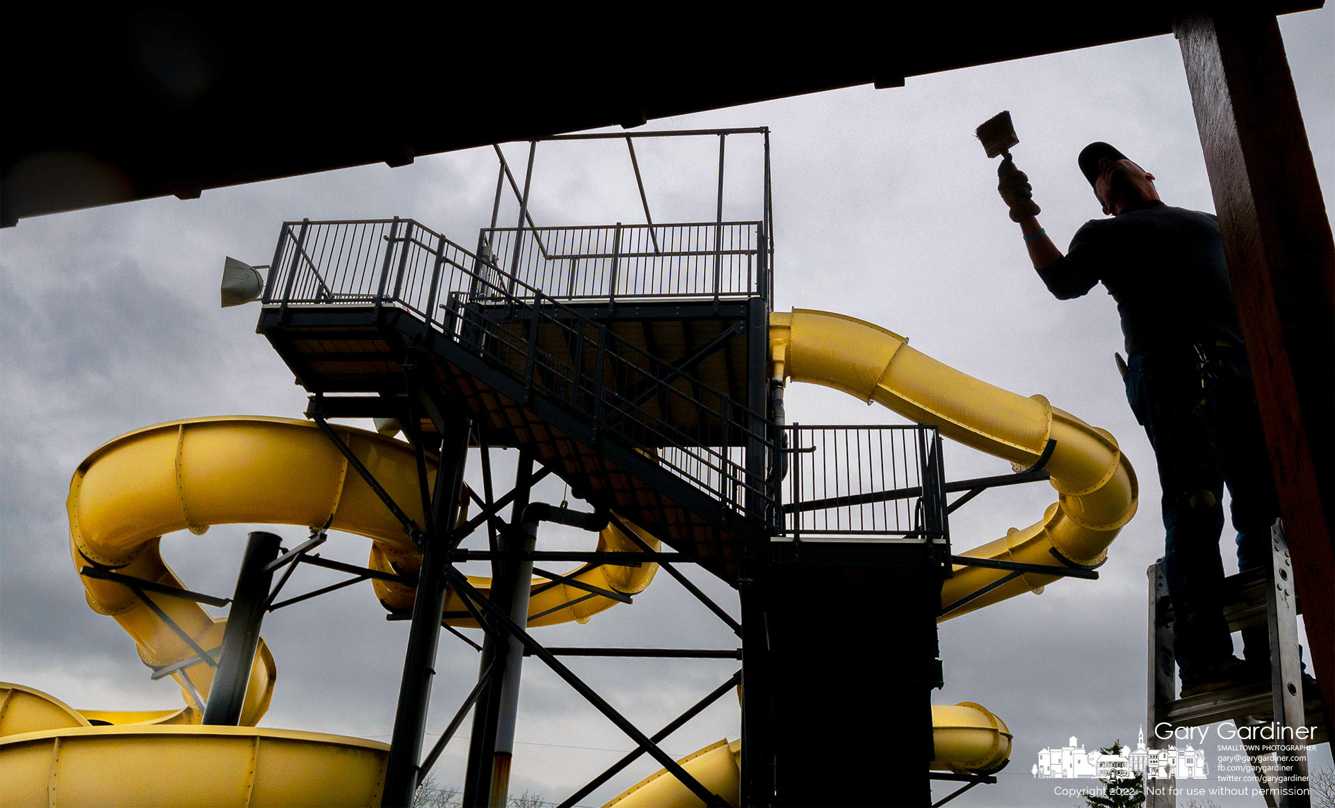 A painter applies stain to a pavilion in the shadow of the slides at Highlands Park Aquatic Center as the pool prepares for its Spring opening. My Final Photo for April 5, 2022. 