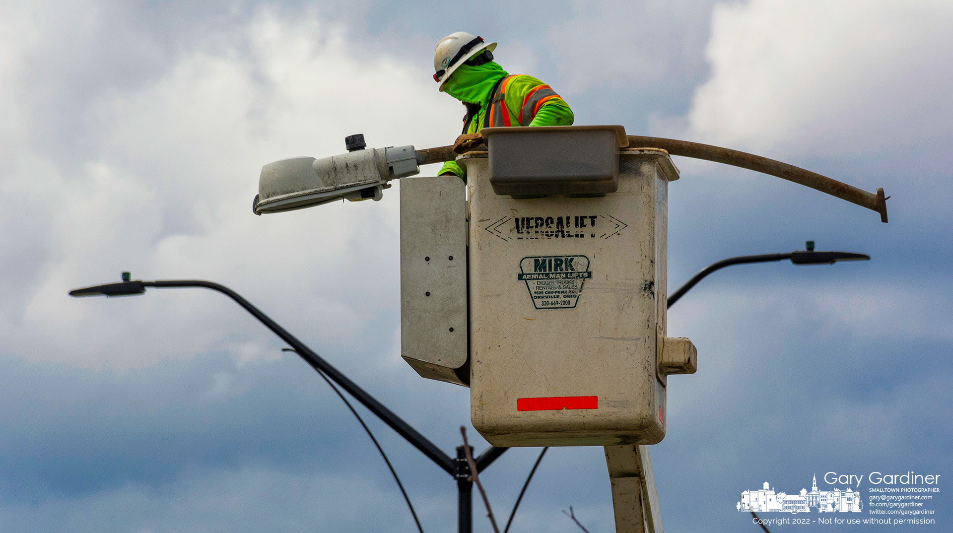 A contractor removes one of the old streetlights from a pole on the berm on Huber Village Boulevard where replacement led lights, in the background, are installed on the medium strip. My Final Photo for March 24, 2022.