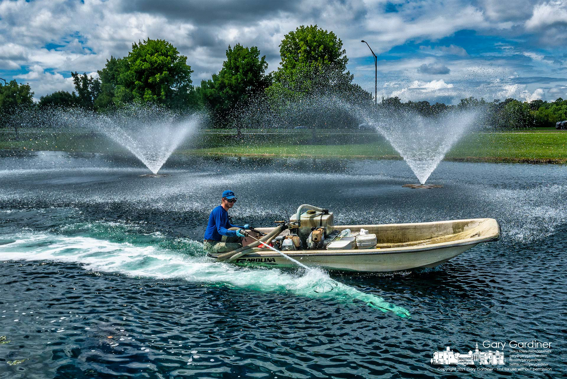 A contractor travels around the pond in front of the Community Center spraying copper sulfate into the water to kill the algae bloom. My Final Photo for Aug. 18, 2021.