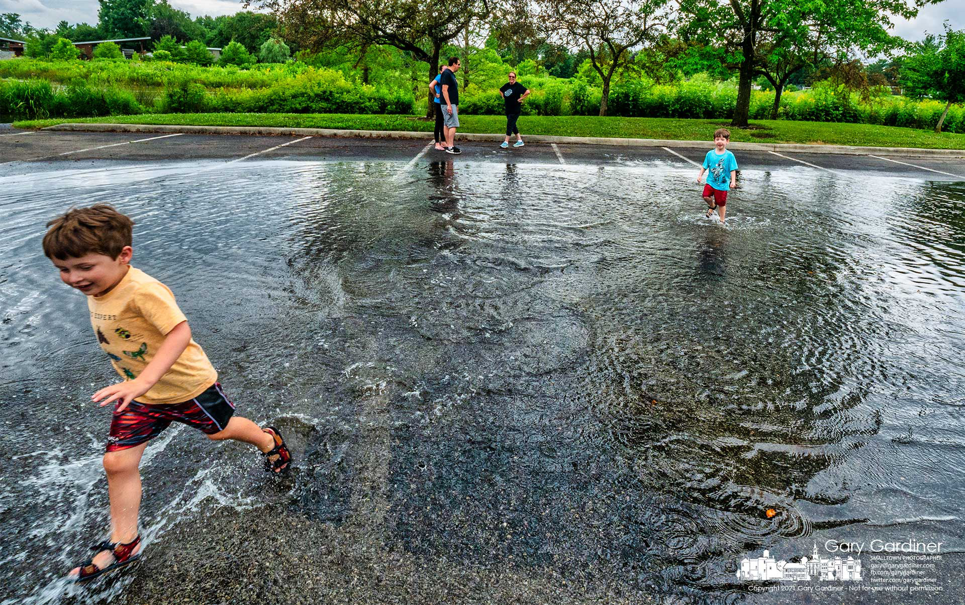 Brothers run through the flooded parking lot at the Highlands wetlands where they earlier trekked along a section of flooded bike path after an afternoon storm brought a brief but heavy rain to parts of the city. My Final Photo for July 11, 2021.