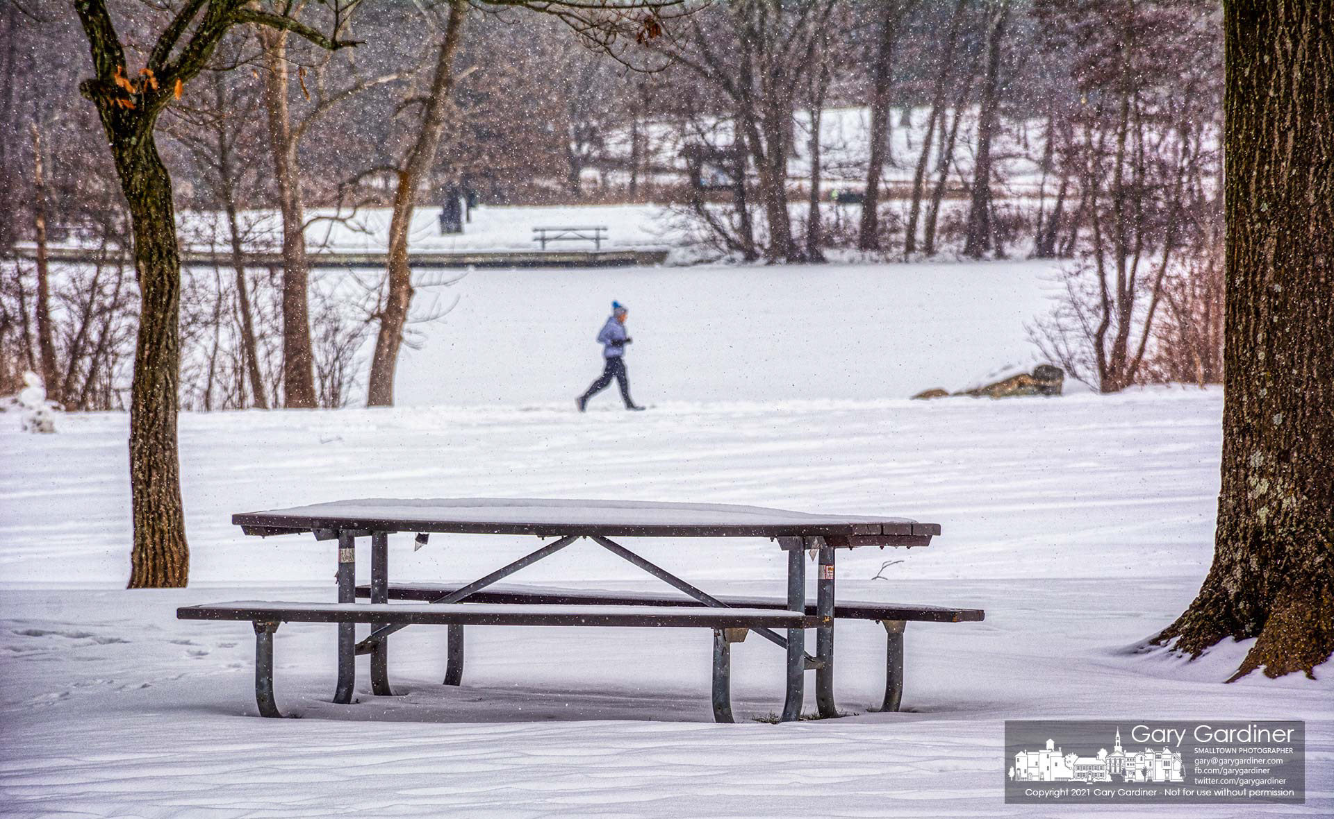 A runner travels along the trail past Schrock Lake at Sharon Woods Metro Park where the picnic tables wear a covering of snow as more is forecast for the week making picnics nearly impossible. My Final Photo for Feb. 13, 2021.