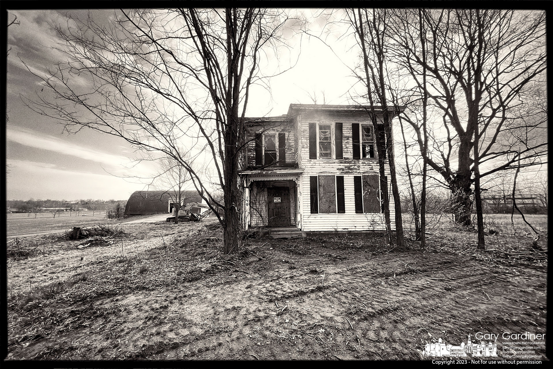 The morning sun breaks over the roofline of the Braun Farm farmhouse where the front yard bears the mark of excavator tracks as the house and barn are prepared for demolition. My Final Photo for April 3, 2023. 