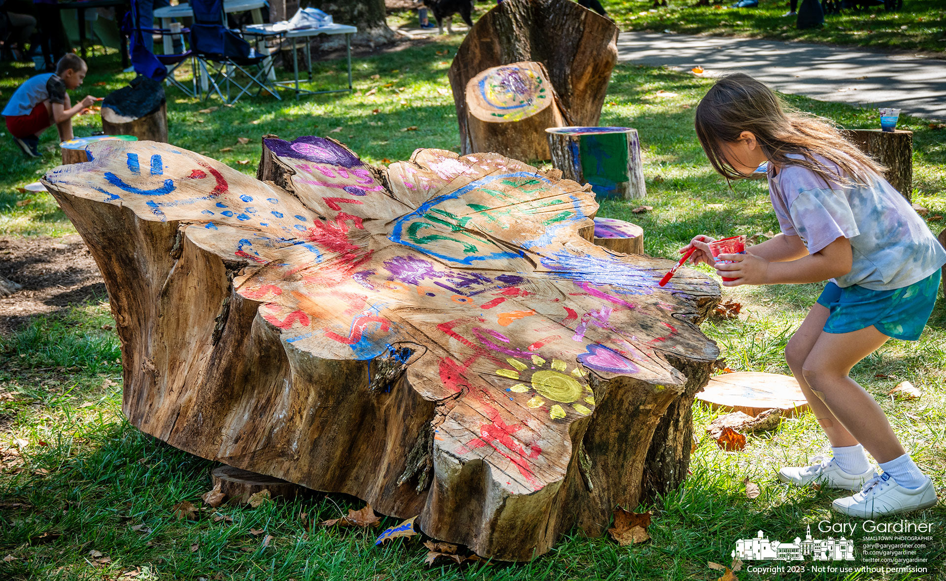 A young girl paints on the upturned stump of the American Elm tree removed this summer from Alum Creek Park North where it returned for Autumn Arborfest. My Final Photo for September 23, 2023. https://bit.ly/456hIGL