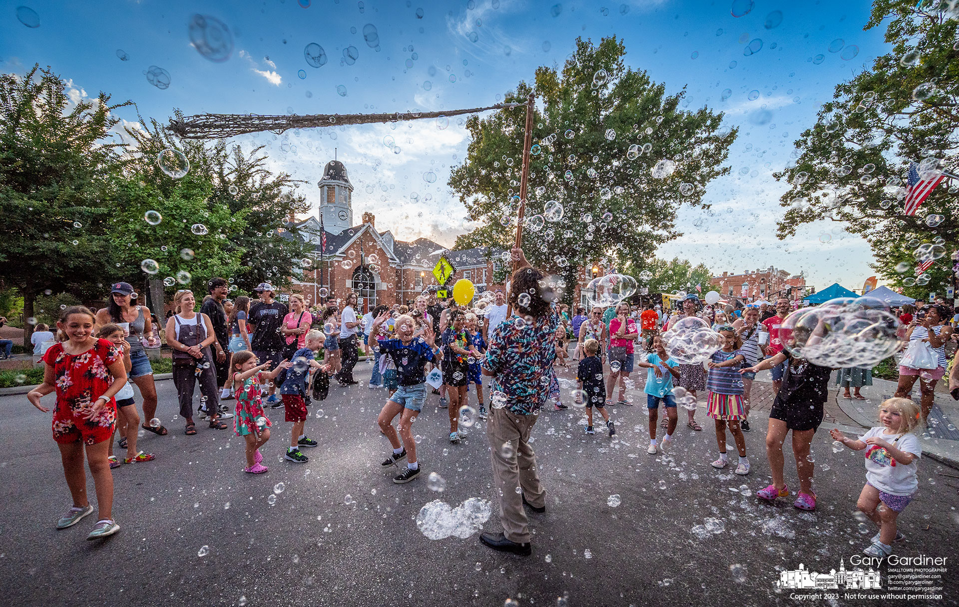 A crowd of kids delight in the explosion of bubbles created by The Giant Bubble Maker on his stop in front of city hall during Fourth Friday in Uptown Westerville. My Final Photo for July 28, 2023. 