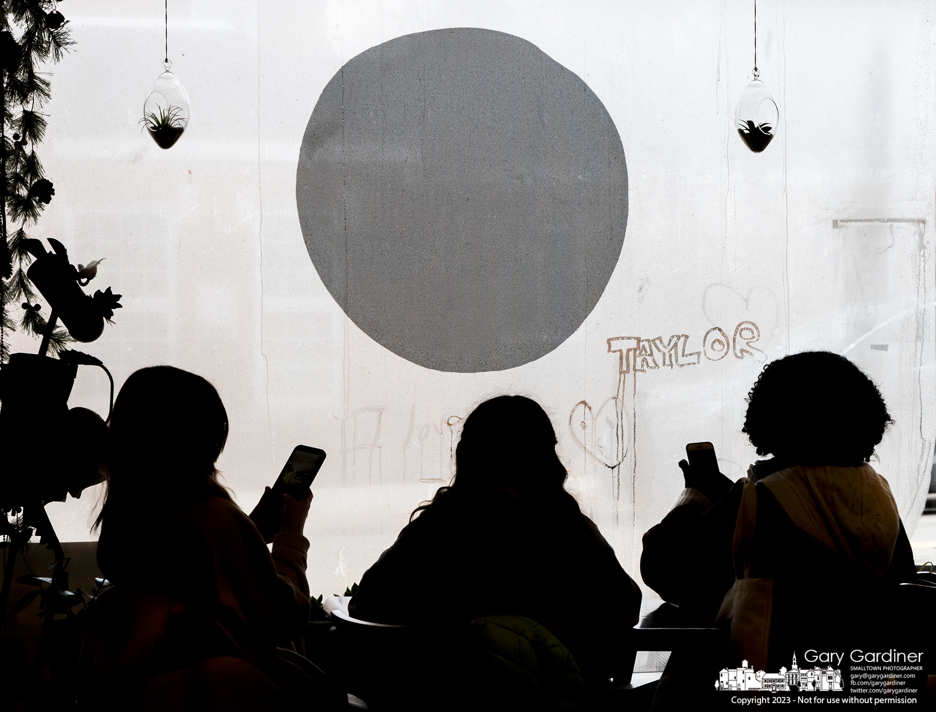 Teenage girls check their phones after writing Taylor Swift's name in the foggy condensation on the front window of Java Central coffee shop in Uptown Westerville. My Final Photo for February 17, 2023.