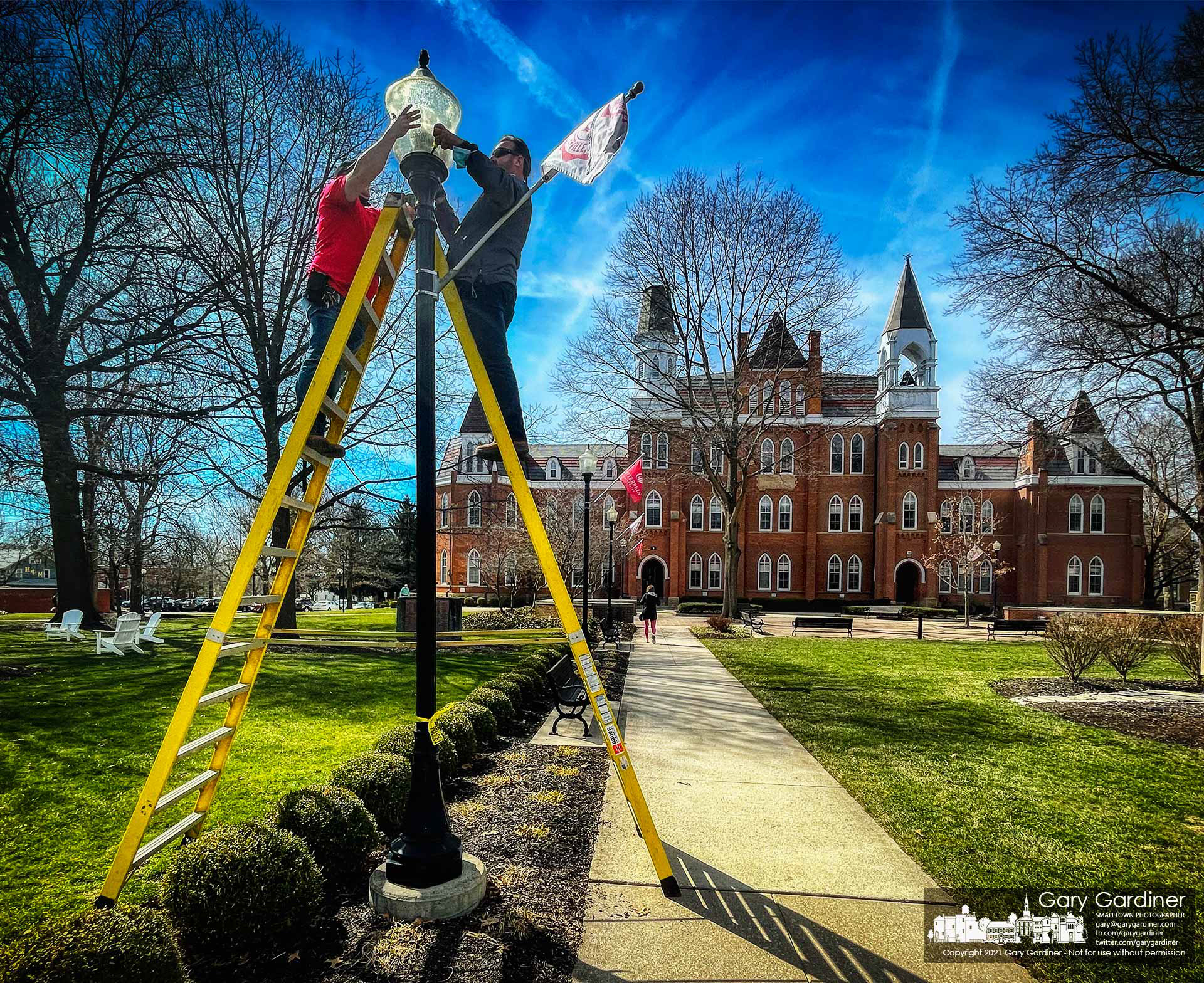 Otterbein maintenance workers replace a bulb in one of the lights illuminating the walkway to Towers Hall at the entrance to the school at the end of College Ave. in Westerville. My Final Photo for March 12, 2021.
