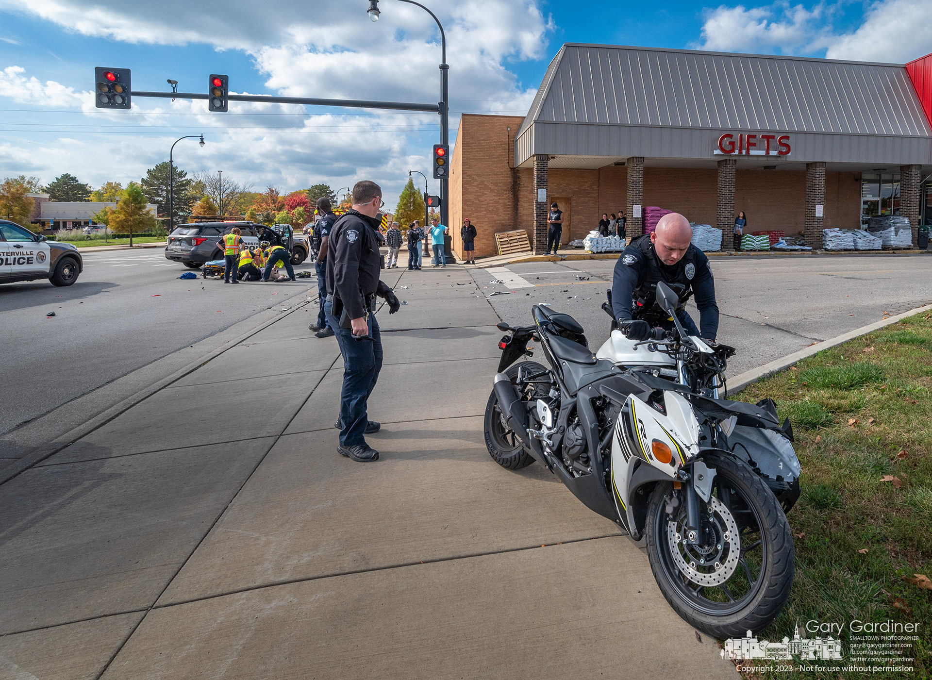 A Westerville police officer removes a motorcycle from Schrock Road where fire department paramedics treat the bike's rider after he struck the side of a truck turniing in front of him. My Final Photo for October 18, 2023. 