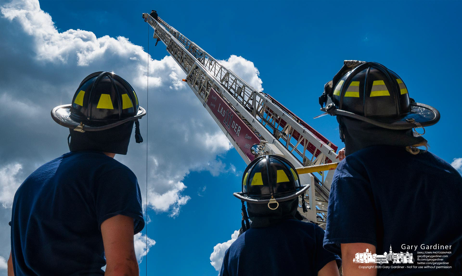 Firefighter trainees watch as another student reaches the top of a 105-foot aerial ladder during training with the climb being the final stage on their exam when training is completed. My Final Photo for June 15, 2021.