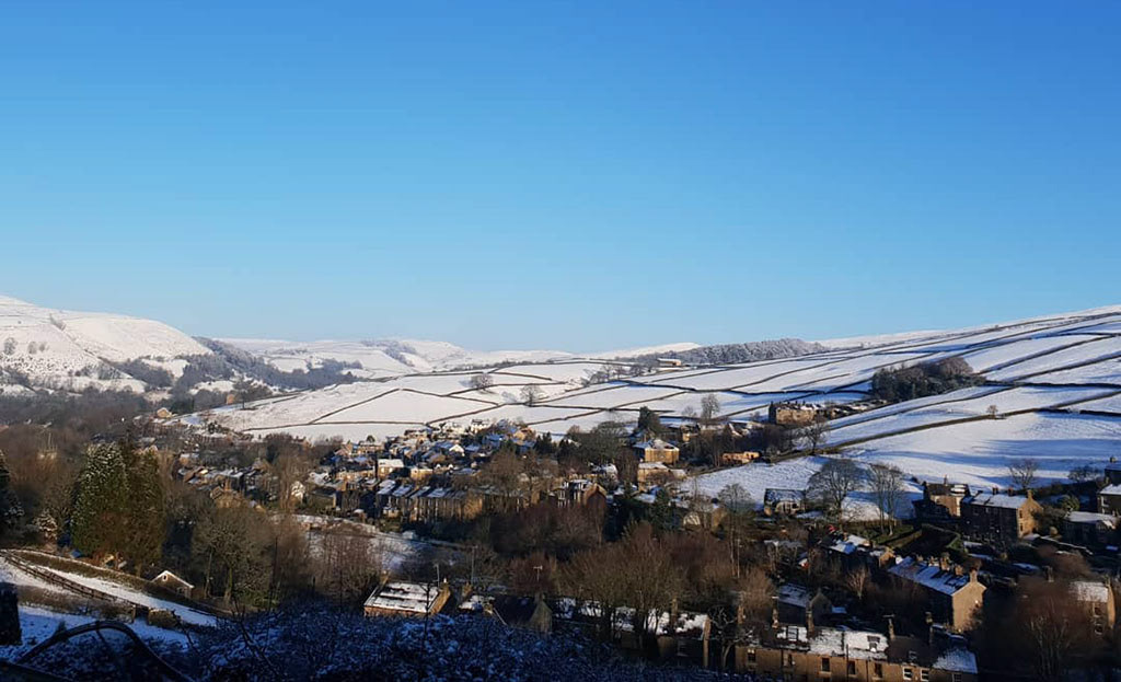 Snowy hills in the Peak District with Hayfield village in the foreground.
