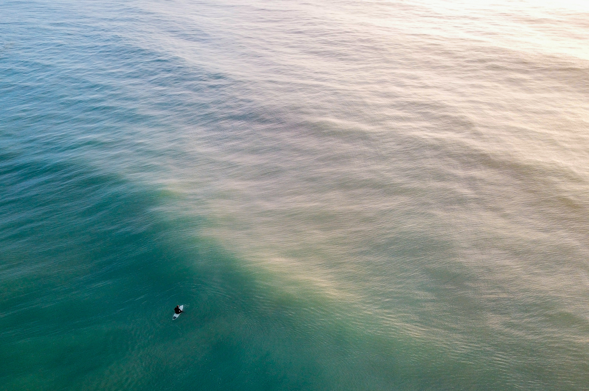 A solo surfer sits on their board off the cost of Dunedin on the South Island of New Zealand on June 14, 2018.