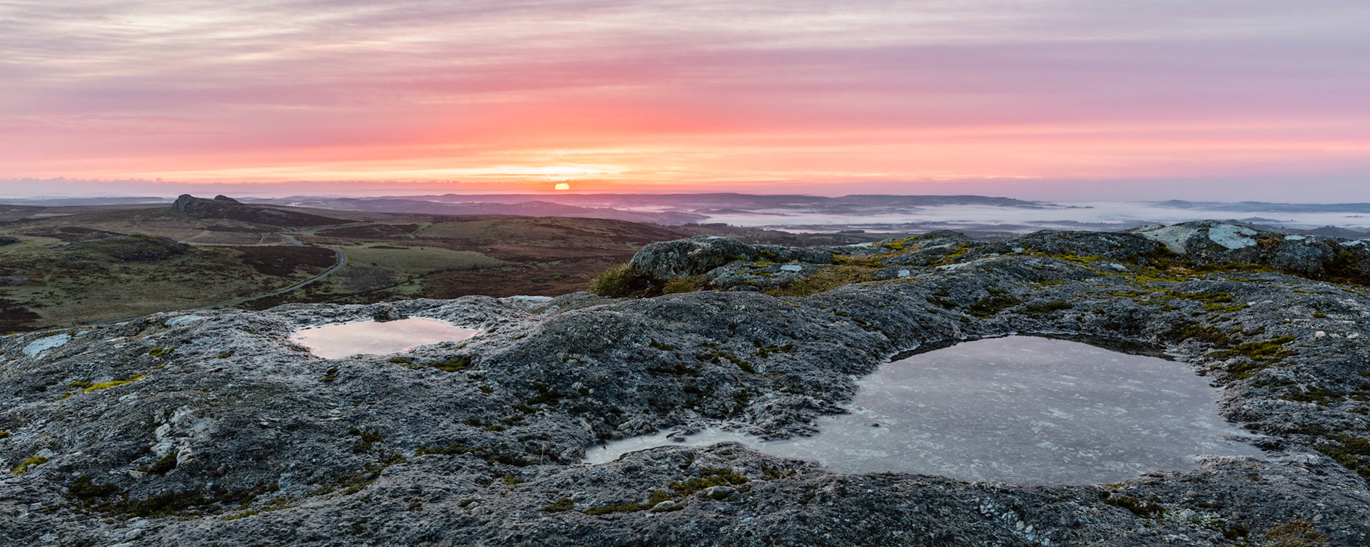 The sun rising above the horizon and giving the clouds a dusting of colour from Rippon Tor in Dartmoor National Park