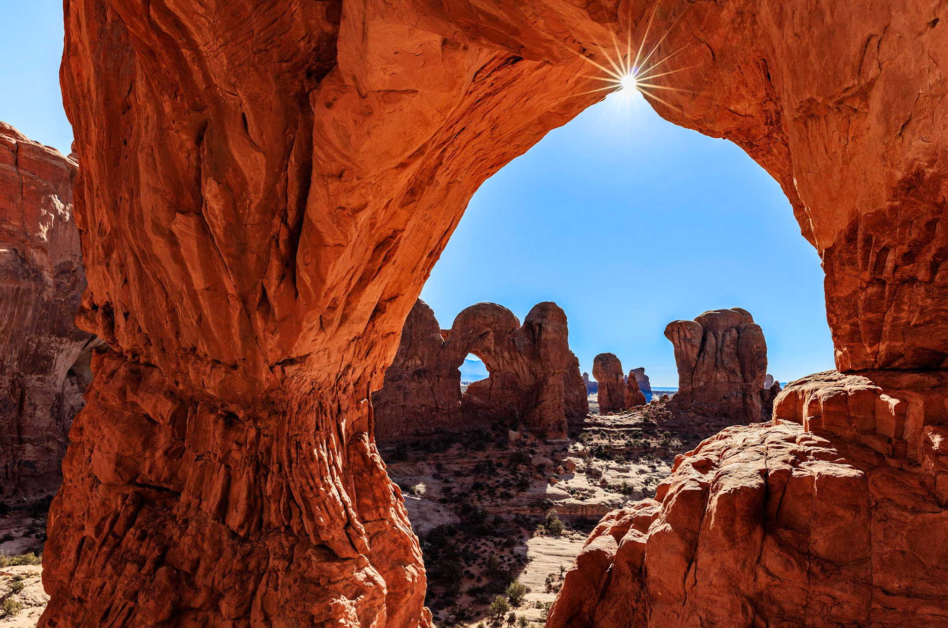 The sun bursting at the pinnacle of Cove Arch looking towards the windows section of Arches National Park, Utah, USA.