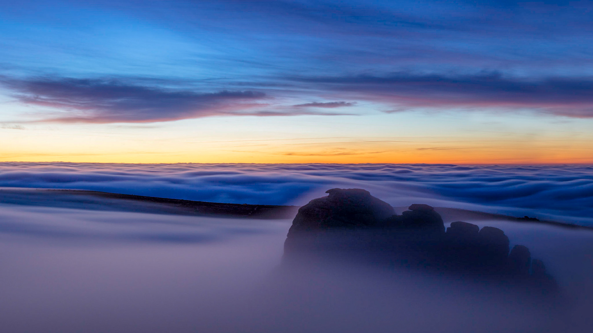 Haytor rocks emerging from the low lying clouds during blue hour in Dartmoor National Park, Devon, England.