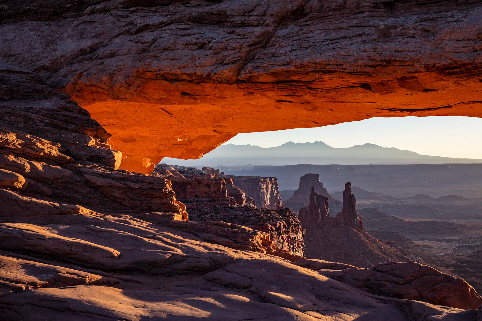 Looking through a glowing Mesa Arch at Washer Woman rock formation and the La Sal Mountain range in the Island of the Sky section of Canyonlands National Park, Utah, USA.