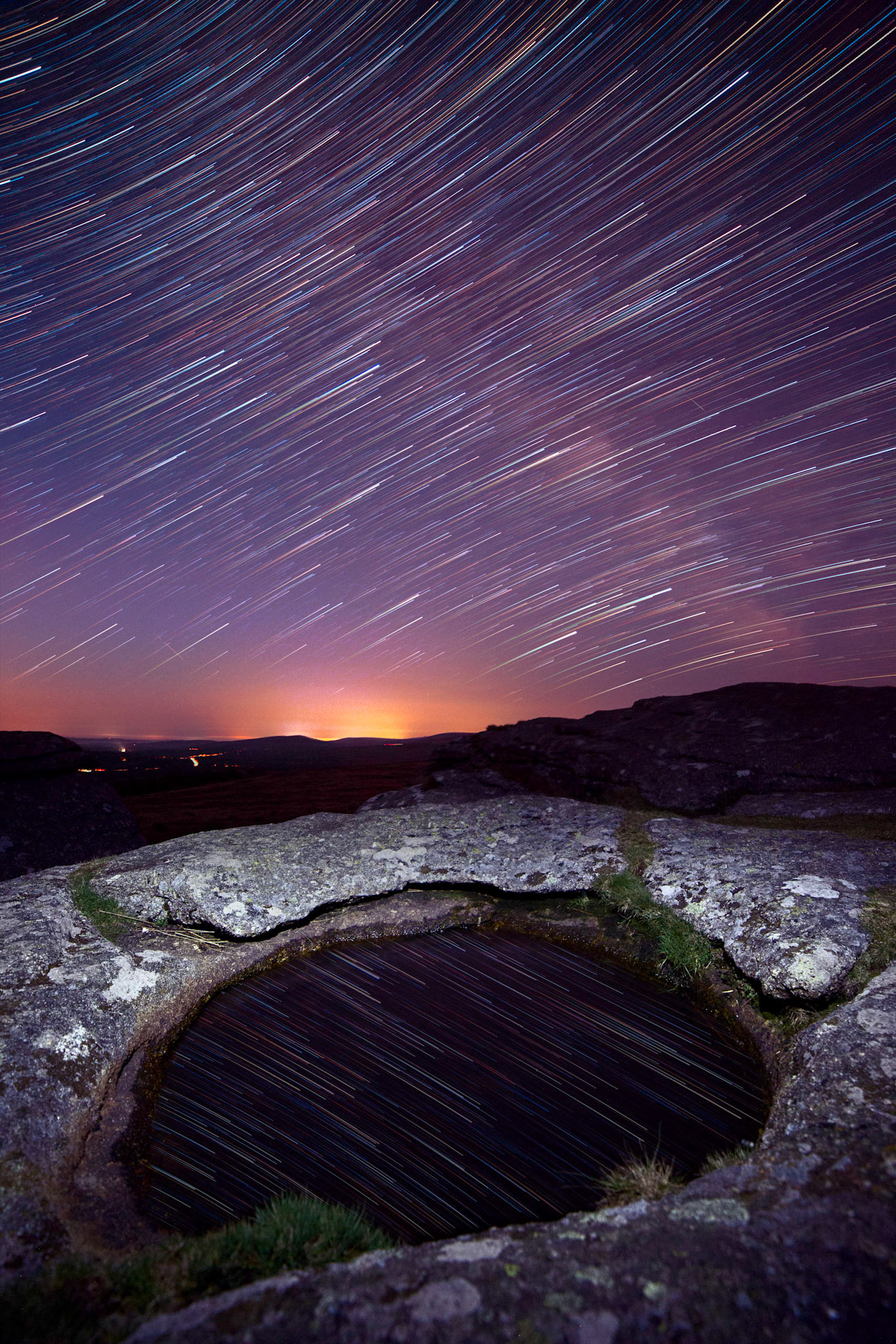 Star trails over a pool of water collected in a depression on Kestor Rocks in Dartmoor National Park.