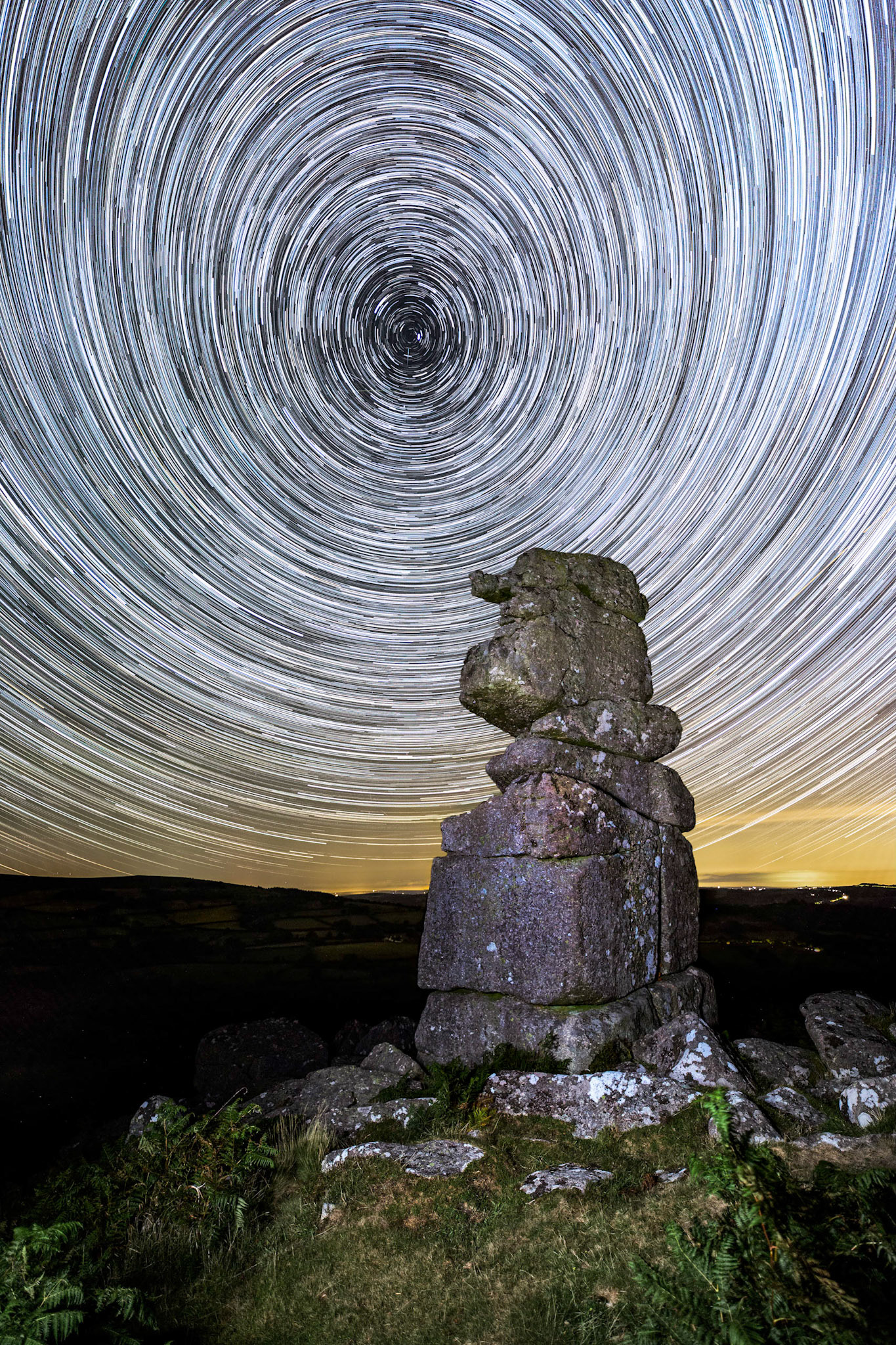 Star trails illuminating the dark dark sky behind Bowerman's Nose (a popular granite rock formation) in Dartmoor National Park, UK