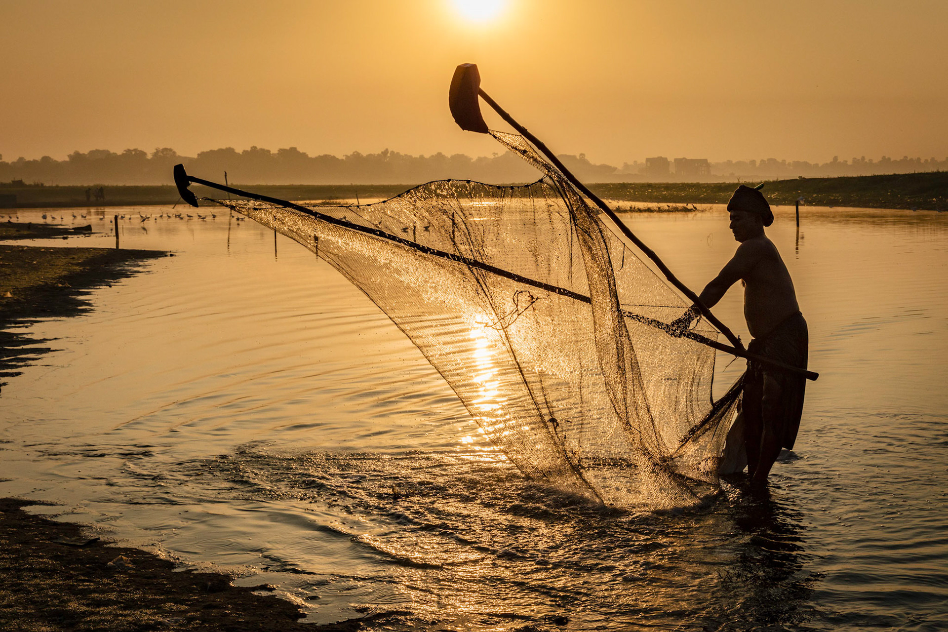 Local Burmese man pushing his fishing net back and forth across the narrow and shallow part of Taung Tha Man Lake during the dry season near U Bein Bridge in Amarapura, Myanmar.