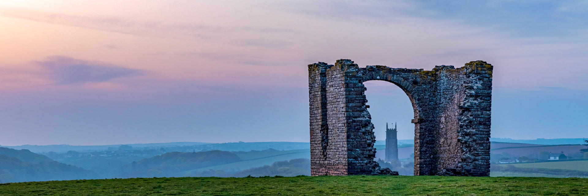 Panoramic view from a hillside near Hartland Quay with the Stoke villiage church tower framed in the arch of a ruined folley.