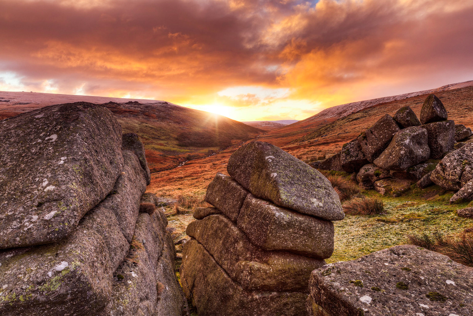Monring sunlight bursting over snow dusted moorland hills of Dartmoor National Park from Shelsone Tor.