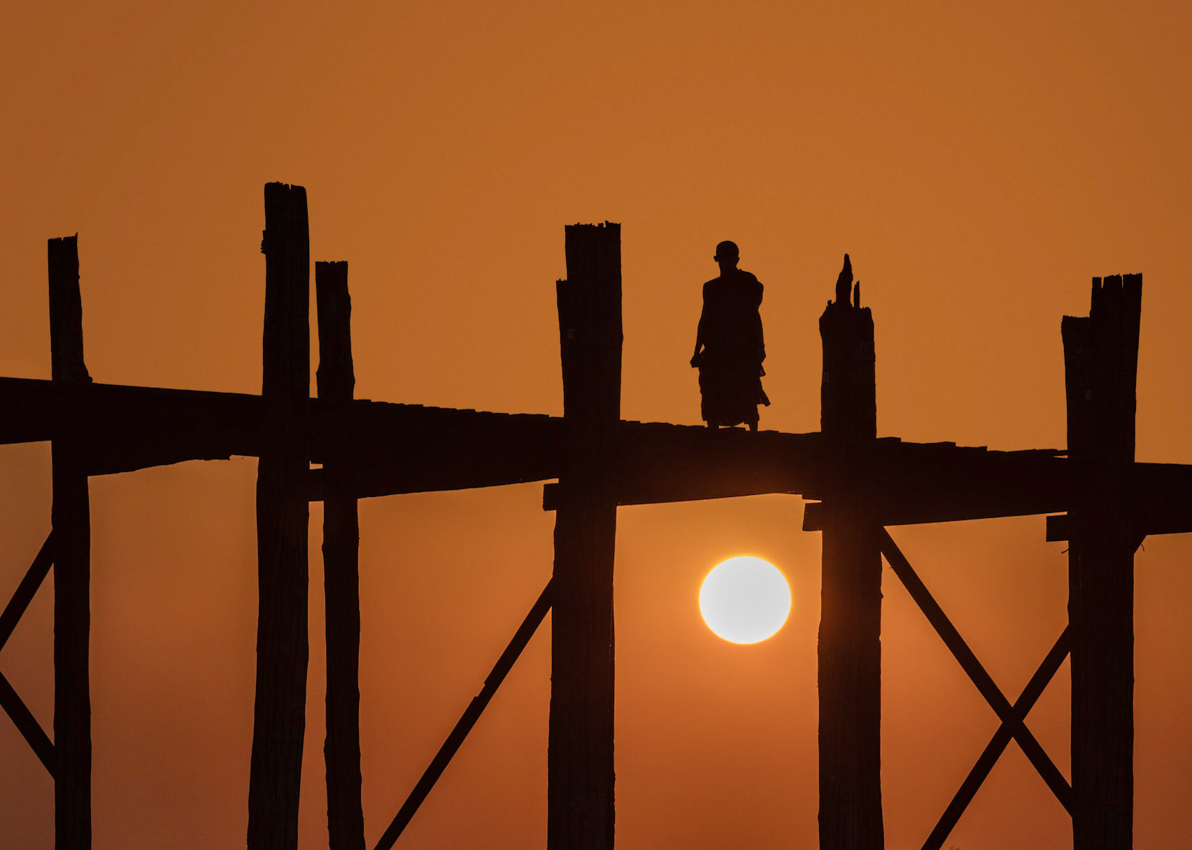 Monk standing alone on the U Bein Bridge watching the sunset in Amarapura, Myanmar.