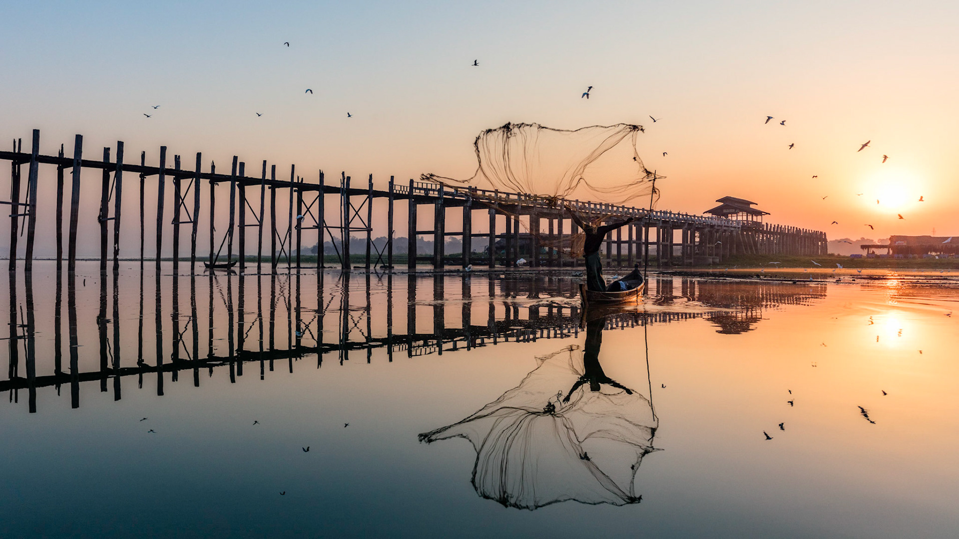 Local Burmese fisherman throwing out his net in the Taung Tha Man Lake with U Bein Bridge in Amarapura, Myanmar.