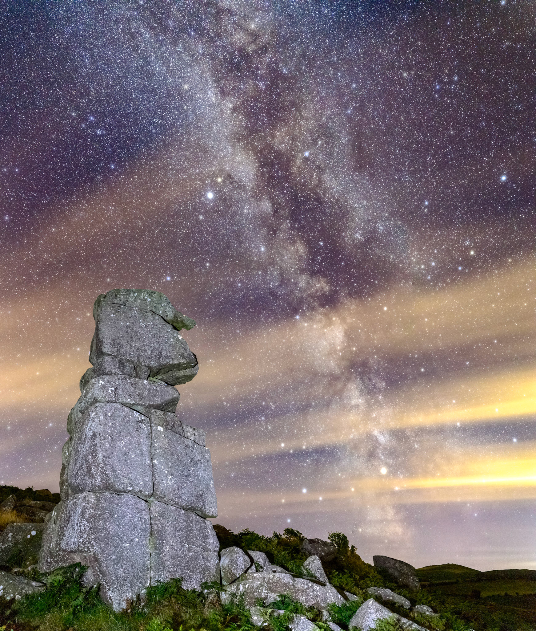 The Milky Way with a few clouds streaking across the sky over Bowerman's Nose in Dartmoor National Park.
