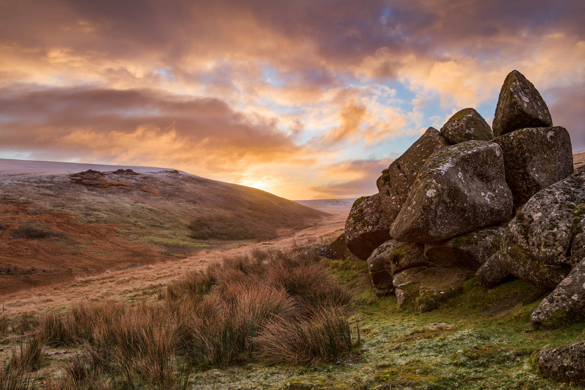 The morning sun illuminating the sky and snow dusting the higher elevations near Shelstone Tor in Dartmoor National Park.
